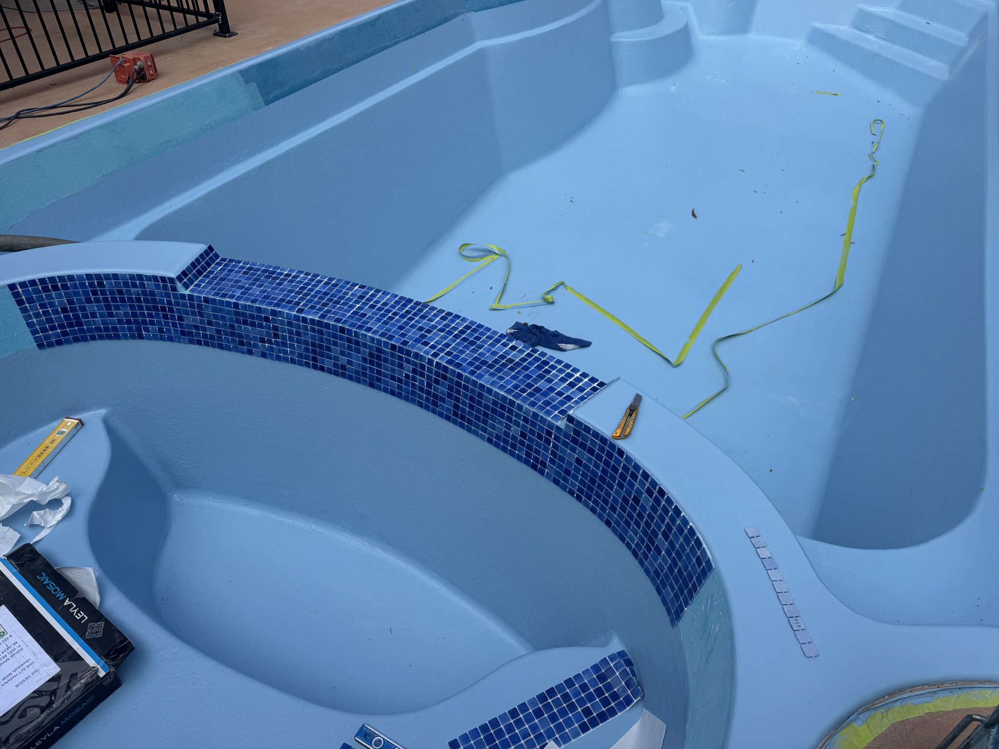 New mosaic waterline tiles being set around a pool