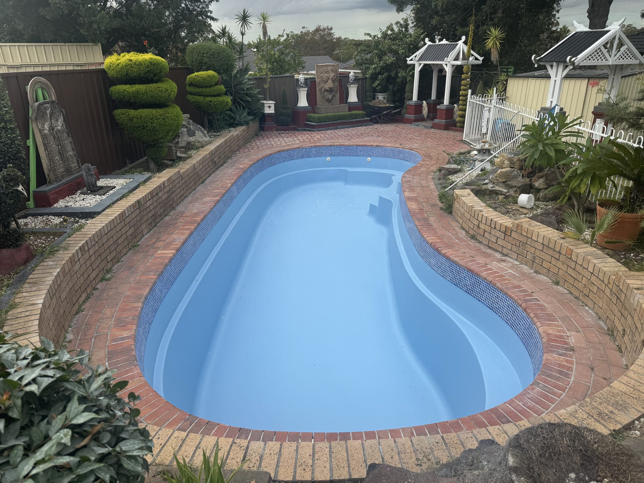 Freeform pool resurfaced in light blue in a landscaped backyard